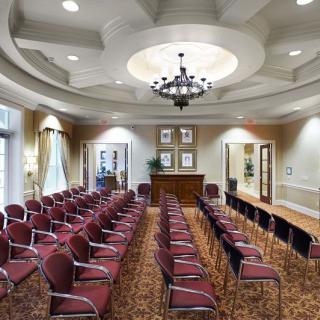 A well-arranged conference room with rows of chairs facing a podium, illuminated by a chandelier.