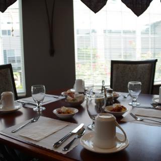 A well-set dining table with cups, glasses, and utensils in a room with large windows.