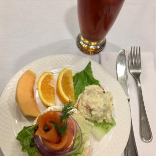 A plate of smoked salmon garnished with greens and served with orange and cantaloupe slices, alongside a glass of iced beverage.