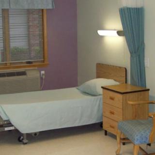 A hospital room with a single bed and bedside furniture.