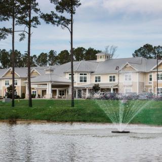 A scenic view of a building by a lake with a fountain and trees.