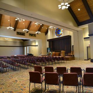An empty auditorium with rows of chairs facing a stage, featuring elegant lighting and a carpeted floor.