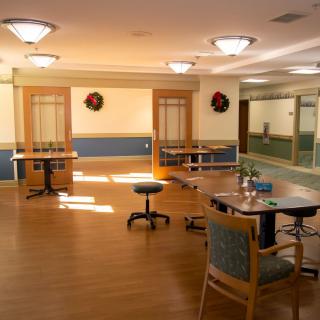 A spacious room with tables and chairs, decorated with wreaths and illuminated by bright ceiling lights.
