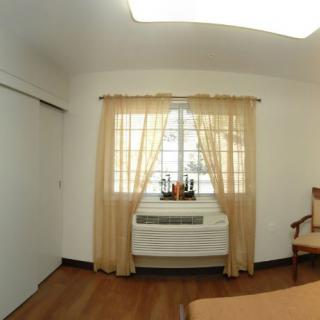 A simple room with a window, beige curtains, and an air conditioner underneath.