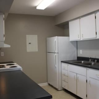 An apartment kitchen with white cabinets, a refrigerator, and a stove.