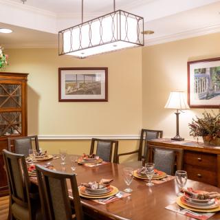 A neatly arranged dining room with a large wooden table, surrounded by chairs, and adorned with elegant decor.