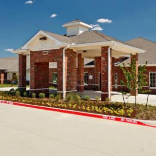 A brick building with a covered entrance, surrounded by landscaping under a clear blue sky.