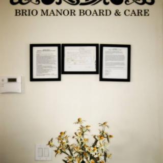 Framed certificates on the wall of Brio Manor Board & Care with a decorative plant below.