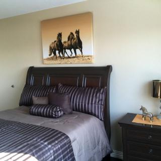 A cozy bedroom featuring a stylish bed with striped bedding and artwork of horses on the wall.