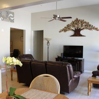 A cozy living room featuring a brown leather sofa set, a television, and decorative wall art under a ceiling fan.