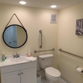 A modern bathroom with a round mirror, sink, and toilet featuring safety grab bars.