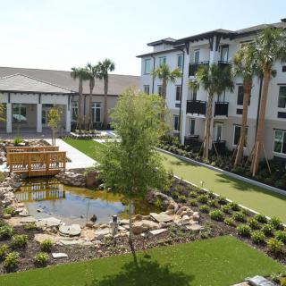 A beautifully landscaped garden with a pond and surrounding modern residential buildings.