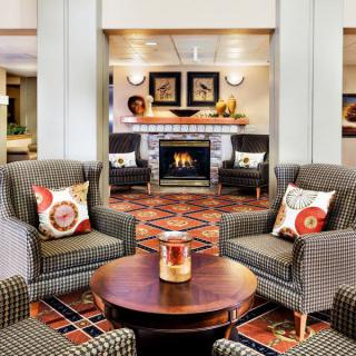 A cozy hotel lobby featuring comfortable seating around a fireplace with decorative pillows and stylish interior design.