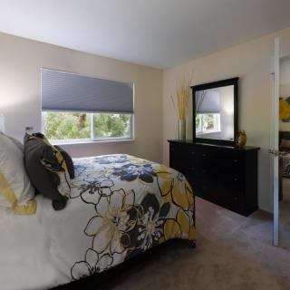 A cozy bedroom featuring a floral bedspread, large mirror, and soft carpeting.