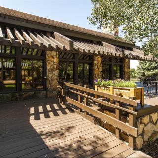 A rustic building with a wooden deck and stone facade surrounded by trees on a sunny day.
