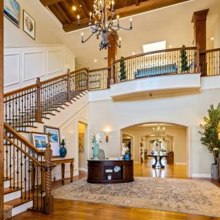 A spacious and elegant foyer with a grand staircase, chandelier, and wood flooring.
