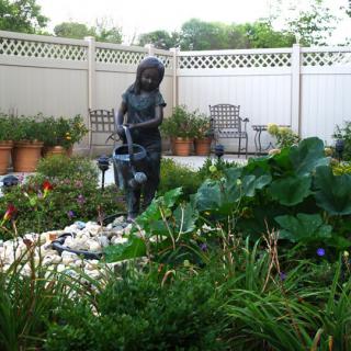 A serene garden featuring a statue of a child with a watering can amidst lush greenery and decorative plants.