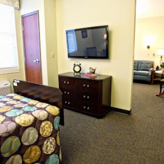 A cozy room featuring a bed with a colorful quilt, a television mounted on the wall, and a dresser, creating a comfortable living space.