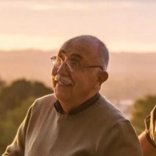 A man standing outdoors, smiling during sunset.