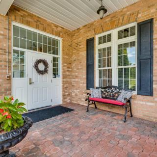 A welcoming front porch with a white door adorned with a wreath, brick walls, and a cozy bench beside potted plants.