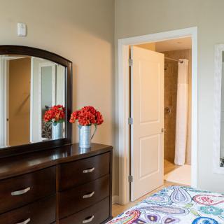 A cozy bedroom with a dresser and mirror, featuring bright red flowers for decoration.