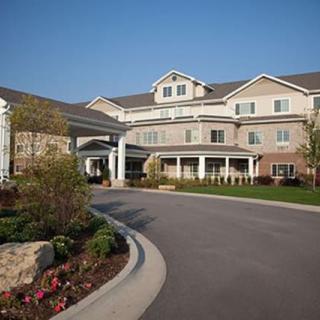 A large residential building with a landscaped entrance and driveway under a clear blue sky.