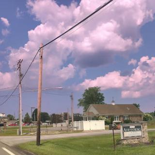 A serene rural scene featuring fluffy clouds and a quaint house under a blue sky.