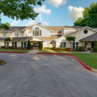A well-maintained residential building with a driveway and landscaped surroundings under a partly cloudy sky.