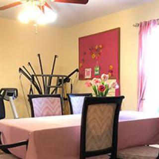 A dining room with a pink tablecloth, flowers, and exercise equipment in the corner.