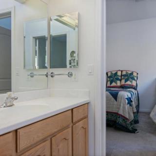 A view of a bathroom with a vanity and mirror, leading into a bedroom with a patterned bedspread.