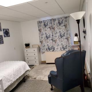 A cozy bedroom with a bed, chair, and dresser, decorated with floral curtains.