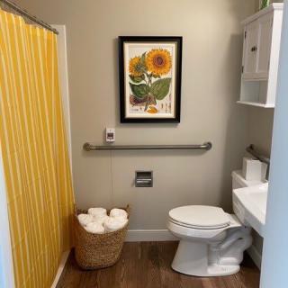 A cozy bathroom featuring a sunflower artwork and yellow shower curtain.