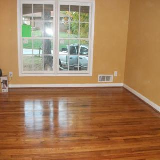 An empty room with a polished hardwood floor and a large window.