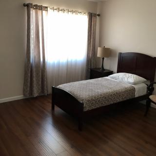 A minimalist bedroom with a single bed, bedside lamp, and large window with curtains.