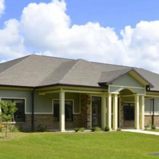 A single-story suburban house with a well-maintained lawn and white columns.
