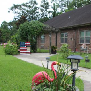 A suburban house with a well-maintained garden, featuring an American flag and a pink flamingo statue near the pathway.
