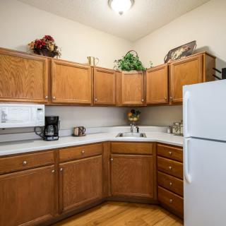 A cozy kitchen corner with wooden cabinets, a refrigerator, microwave, and coffee maker.