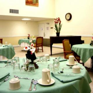 A neatly set dining area with tables covered in green tablecloths, featuring floral centerpieces.