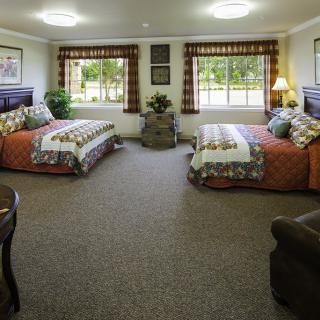 A spacious hotel room featuring two twin beds with colorful bedding and large windows allowing natural light.