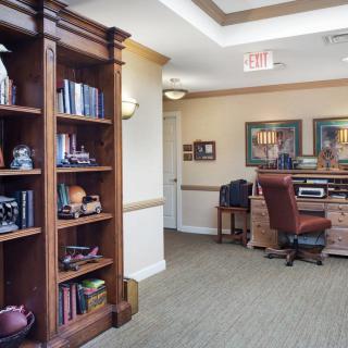 A cozy office space with a wooden bookshelf and desk, featuring decorative items and comfortable seating.