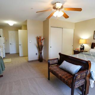 A cozy bedroom with a ceiling fan, featuring a comfortable bed and a decorative bench.