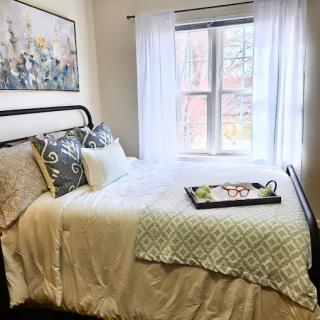 A cozy bedroom filled with natural light, featuring a neatly made bed and decorative pillows.