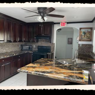 A modern kitchen with dark wood cabinets, a marble countertop island, and a ceiling fan.