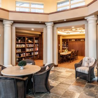 A cozy library with bookshelves, a reading area, and classic columns surrounding a round table.