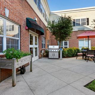 A cozy outdoor patio area with a grill and seating, adjacent to a brick building.