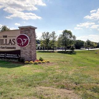 Entrance sign for The Villas at a residential complex surrounded by grass and trees under a blue sky.