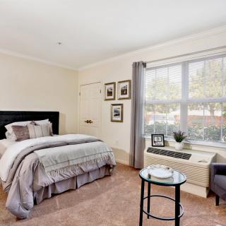 A cozy bedroom with a neatly made bed, large window, and simple decor.