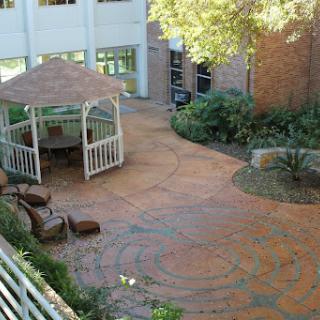 A serene courtyard featuring a gazebo surrounded by lush greenery and a patterned walkway.
