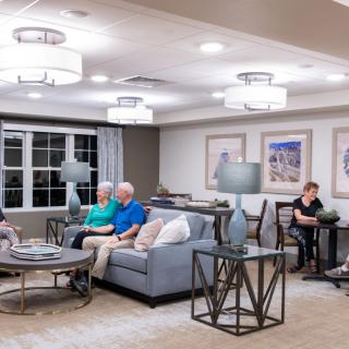A cozy living room with several people seated on sofas, enjoying a relaxed atmosphere under modern lighting.
