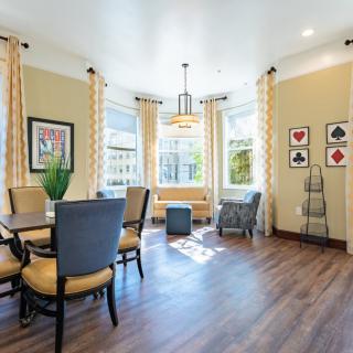A well-lit living room with chairs around a table, large windows with curtains, and stylish decor.